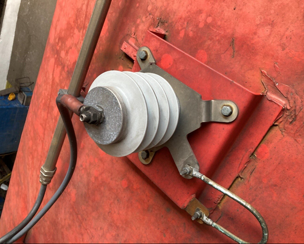 Grafika przedstawia odgromnik zaworowy. Ma on kształt żebrowanego walca. Na jego górnej podstawie znajduje się miejsce przyłączenia przewodu. Odgromnik przymocowany jest do obudowy pociągu przy pomocy śrub.