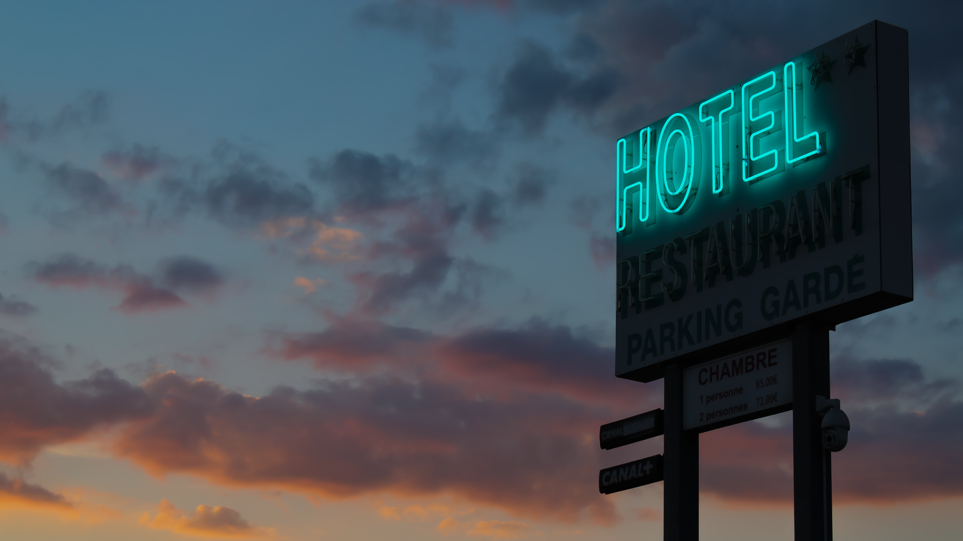 Zdjęcie przedstawia billboard, na którym znajduje się neon z napisem: Hotel. W tle widoczne są chmury na niebie. Niebo wygląda jak przy zachodzie słońca.
