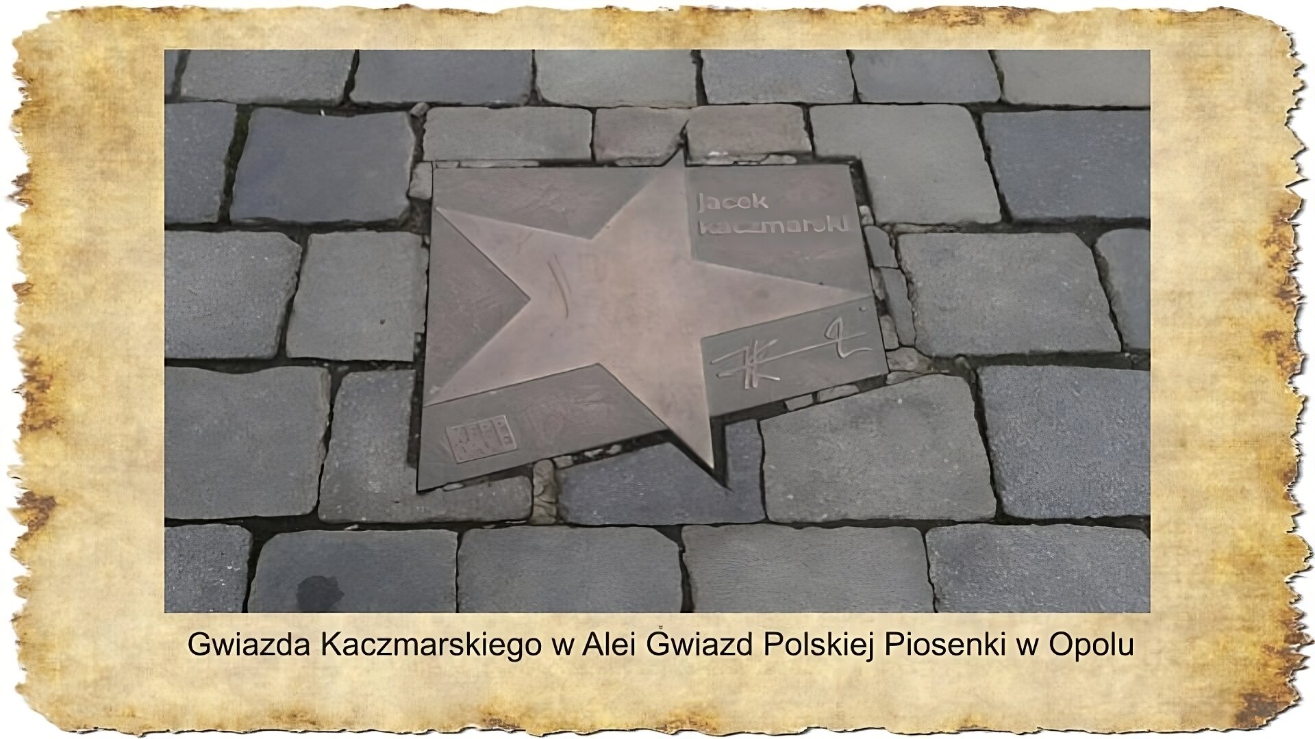 Na slajdzie widoczna jest fotografia przedstawiająca tabliczkę z gwiazdą obok której widnieje napis Jacek Kaczmarski. Tabliczka umieszczona jest między płytami chodnikowymi. Pod zdjęciem podpis: Gwiazda Kaczmarskiego w Ali Gwiazd Polskiej Piosenki w Opolu.