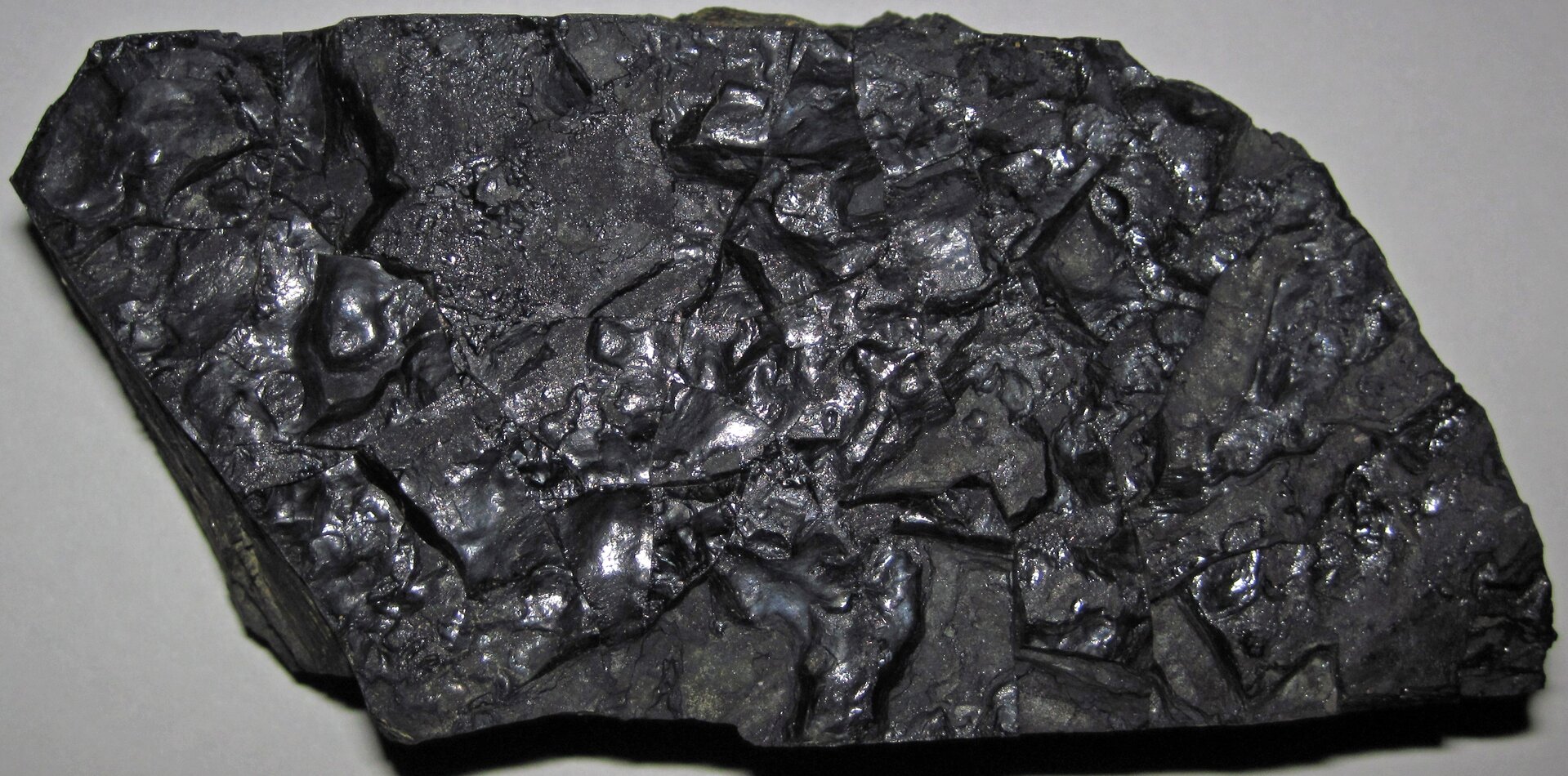 Zdjęcie przedstawiające kawałek węgla kamiennego. Jest to czarna połyskliwa skała pochodzenia roślinnego.