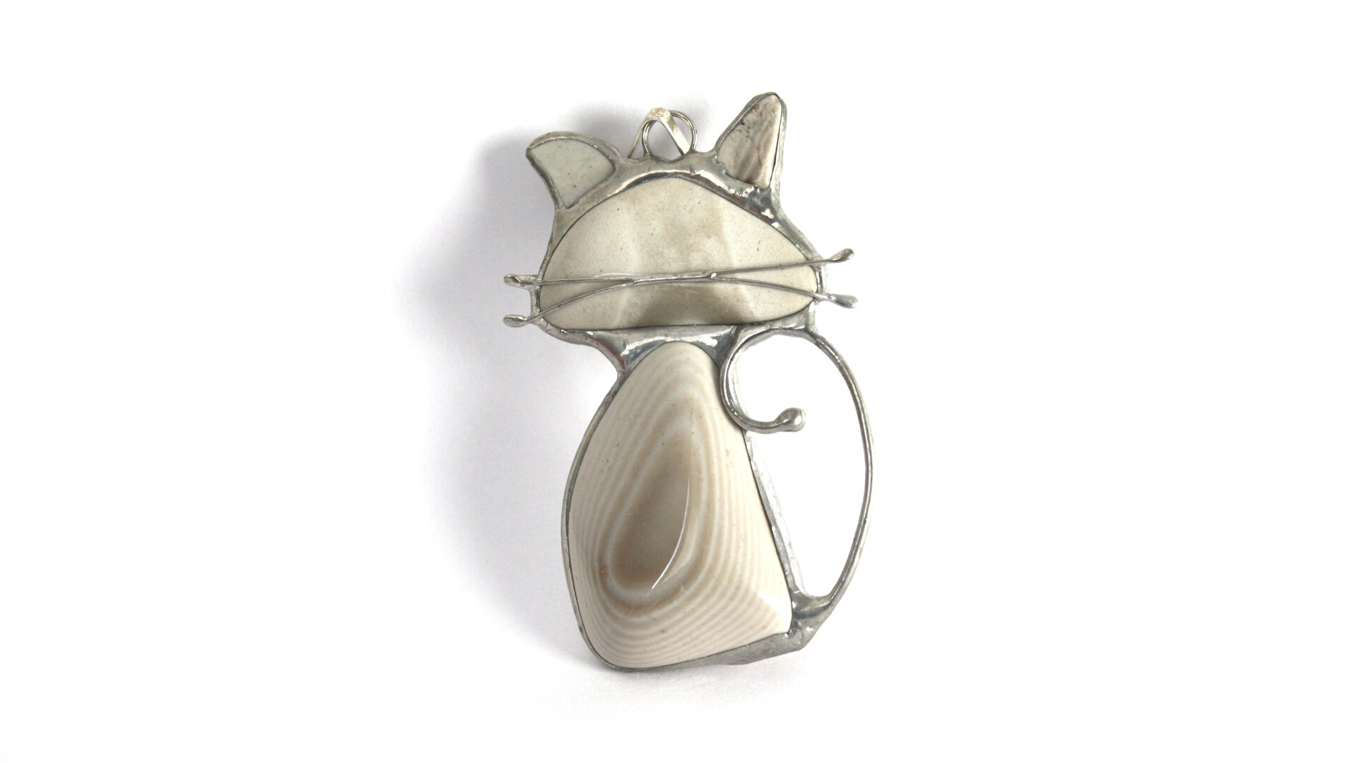 Zdjęcie przedstawia przykład biżuterii z krzemienia pasiastego, naszyjnik. W metalową, przypuszczalnie srebrną oprawkę w kształcie kotka wprawiono cztery kawałki krzemienia pasiastego. Największy, o wyraźnym biało beżowym wzorze tworzy brzuch kota, nieco mniejszy beżowy to głowa, a dwa najmniejsze wypełniają przestrzeń na uszy. Kotek ma również wąsy zrobione z dwóch drucików zlutowanych z resztą metalowej oprawki i przyklejonych do kamienia.