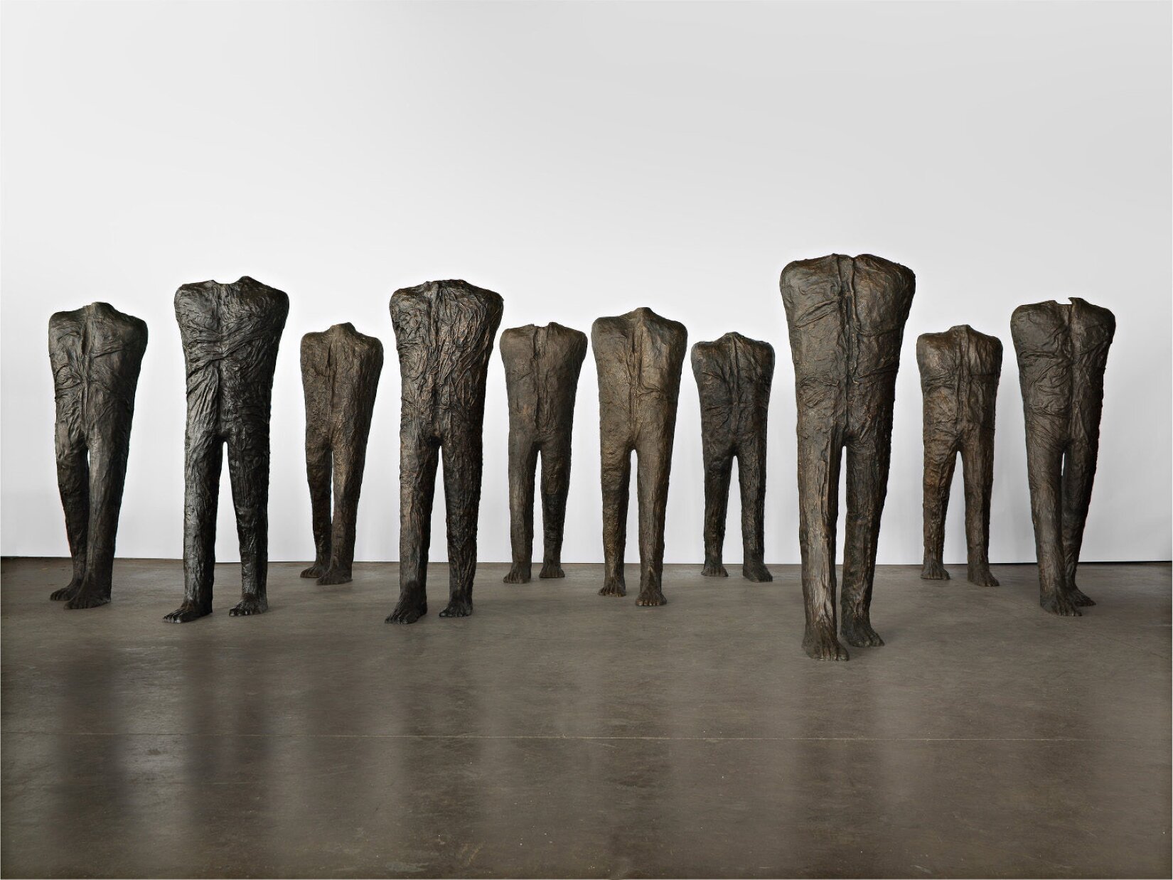 Praca przedstawia figury wykonane z materiału, pozbawione rąk i głów. Każda z figur znajduje się ruchu i jest ich 10.