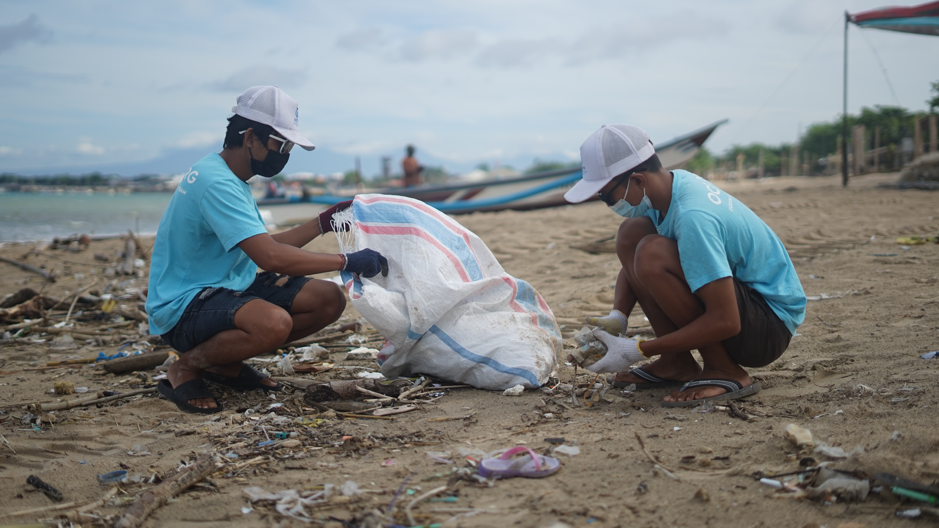 Zdjęcie przedstawia dwóch wolontariuszy sprzątających śmieci na plaży do worka.