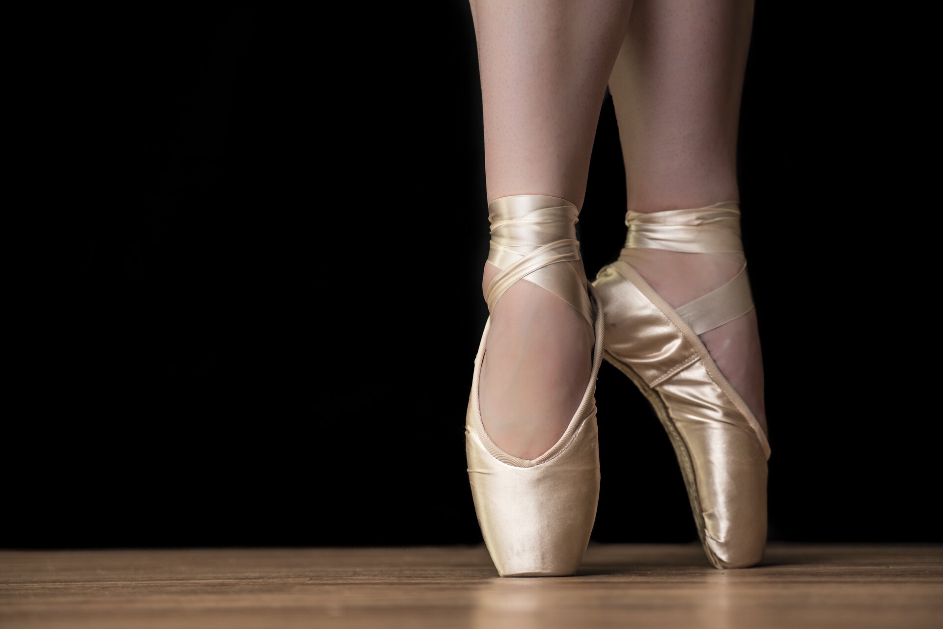 Ilustracja przedstawia stopy tancerki baletowej w pointach zwanymi także baletkami. Są one w kolorze złotym. Kobieta stoi na palcach.
