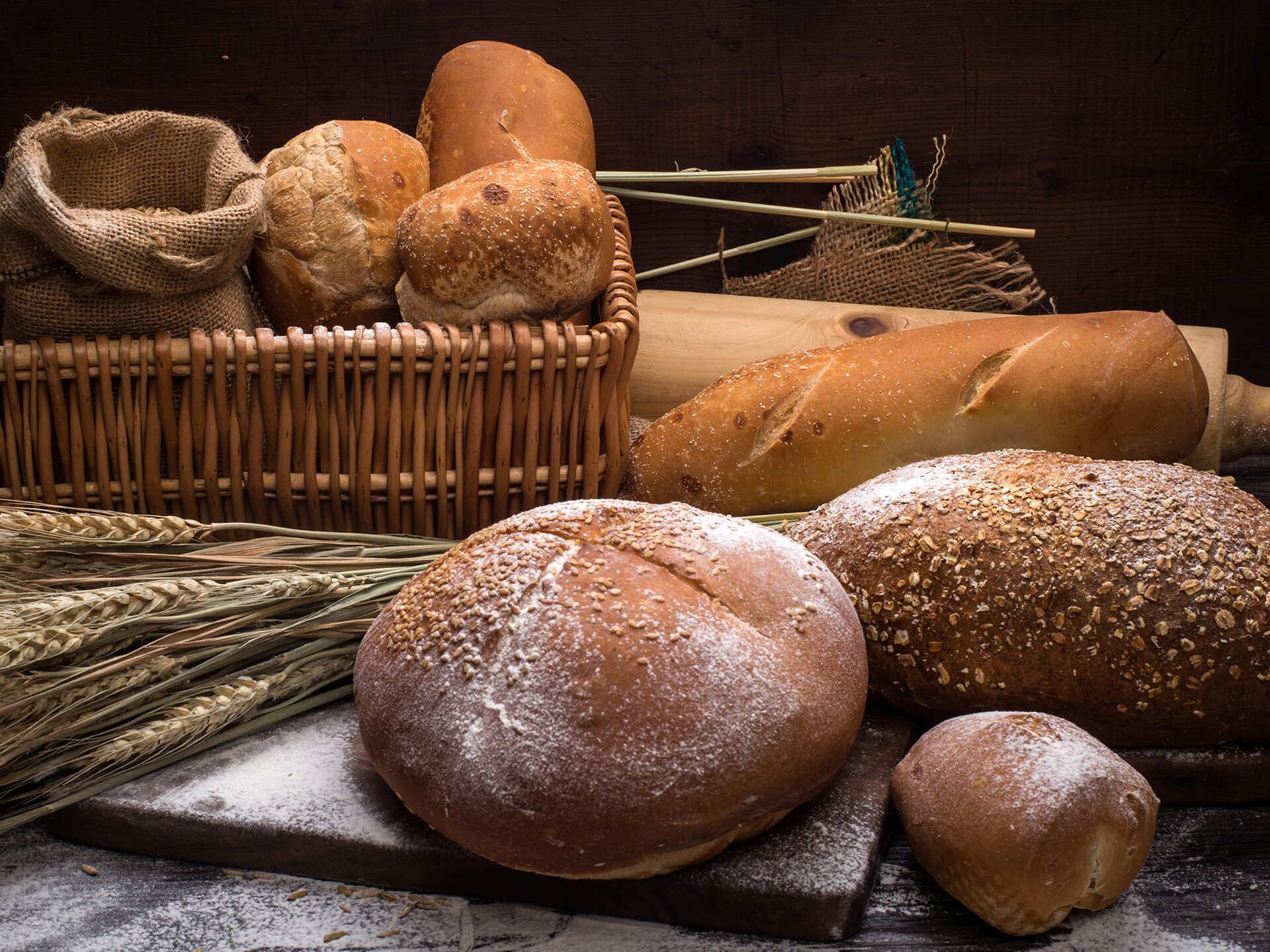 Zdjęcie przedstawia wyroby z piekarni. Widoczne są bochenki chleba, bułki i bagietka. Pomiędzy nimi widzimy kłosy zboża.