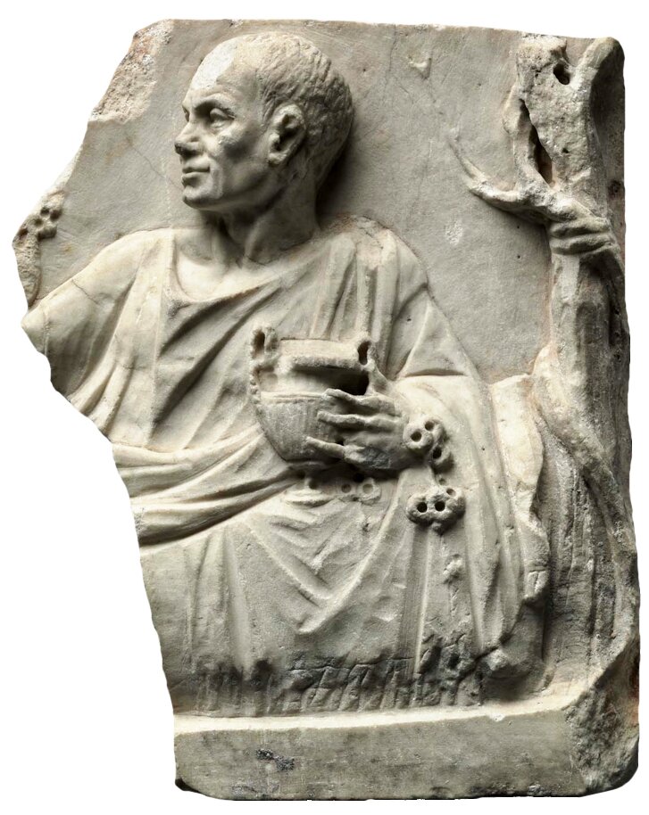 Ilustracja przedstawia marmurową tablicę z ukruszonym lewym górnym brzegiem. Na niej wyrzeźbiona postać mężczyzny w średnim wieku. Ma krótkie proste włosy, jest ubrany w szatę z długimi szerokimi rękawami, siedzi wygodnie oparty, głowę ma zwróconą w lewo, widzimy jego lewy profil. Ma zadowolony wyraz twarzy, w lewej ręce trzyma ozdobny kielich.