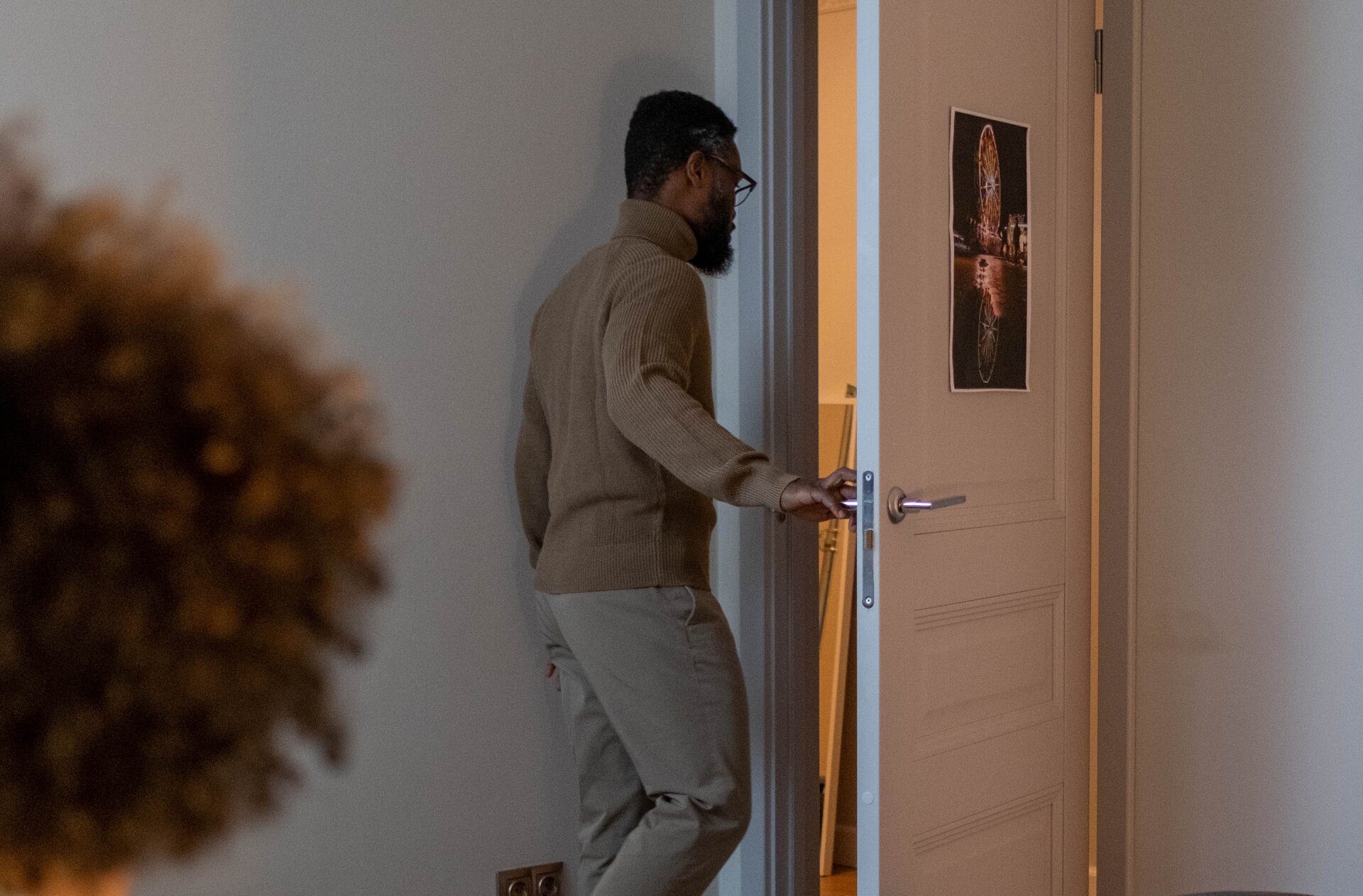 Zdjęcie przedstawia mężczyznę wychodzącego z mieszkania i zamykającego za sobą drzwi.