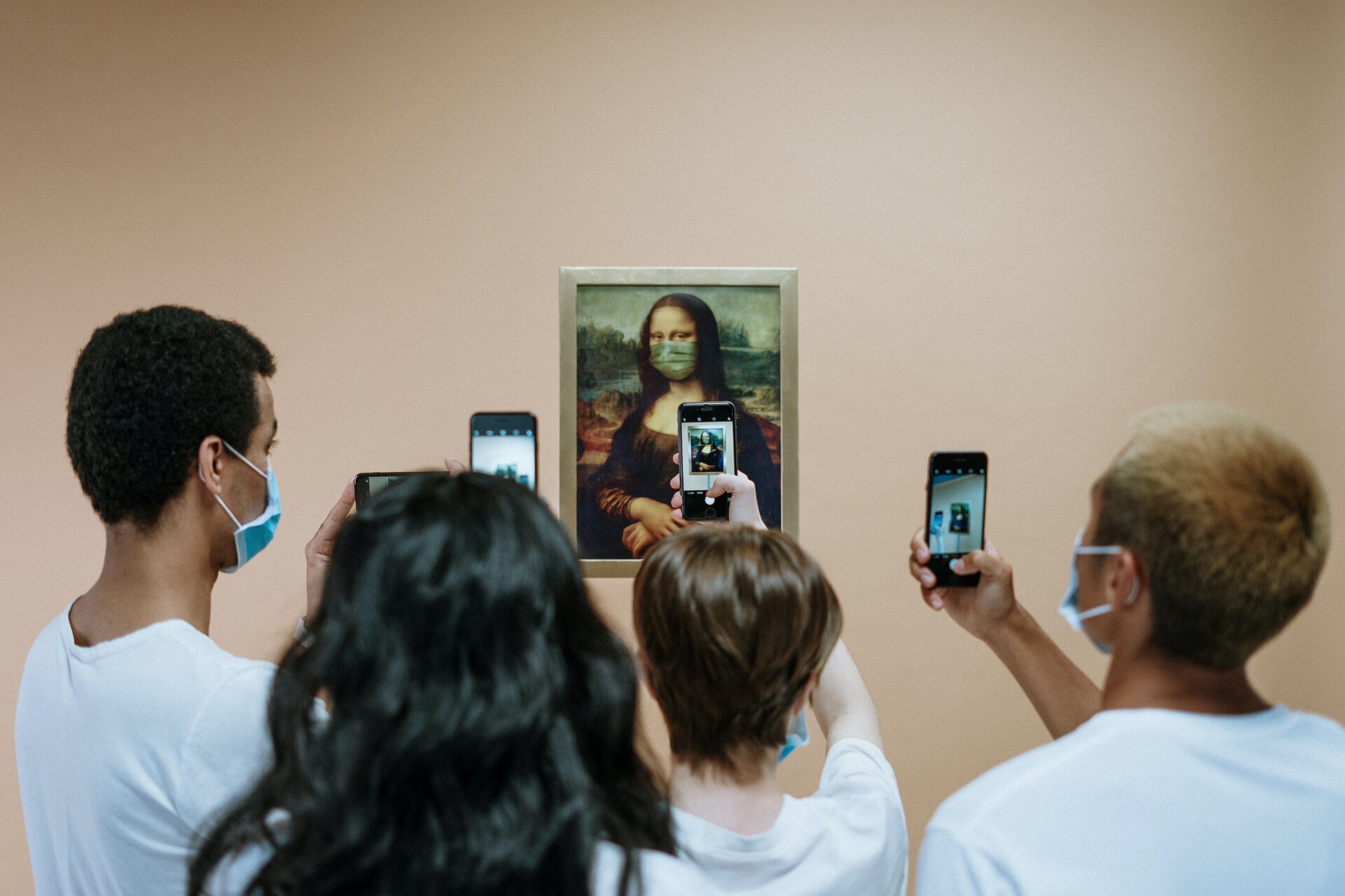 Zdjęcie przedstawia przykładowe użycie aplikacji Google Goggles w muzeum. Na zdjęciu widać od tyłu cztery osoby, skierowane ku obrazowi zmodyfikowanej kopii Mona Lisy z maseczką na twarzy, który wisi na beżowej ścianie. Osoby trzymają w podniesionych rękach telefony komórkowe, których ekrany skierowane są na obraz.