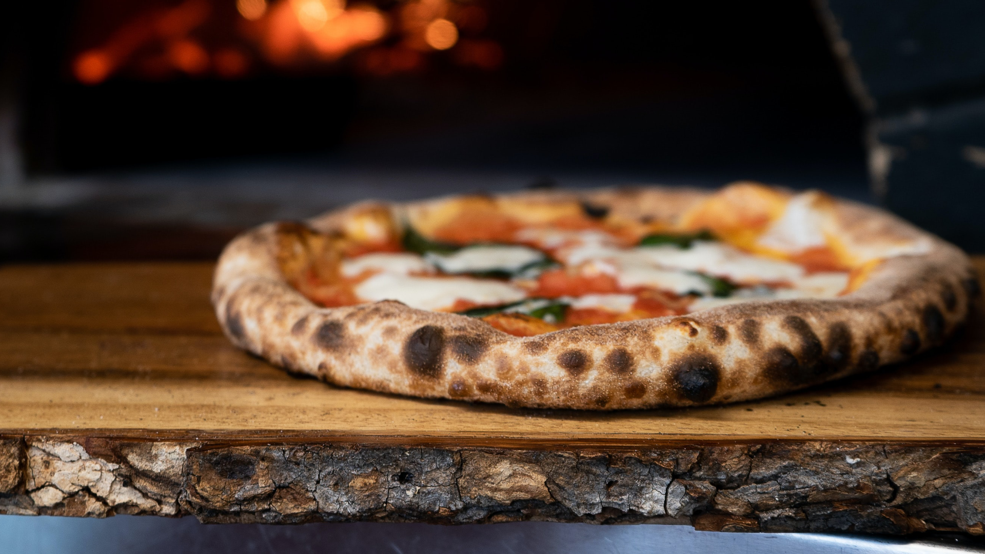 Zdjęcie przedstawia wypieczoną pizzę leżącą na drewnianym blacie.