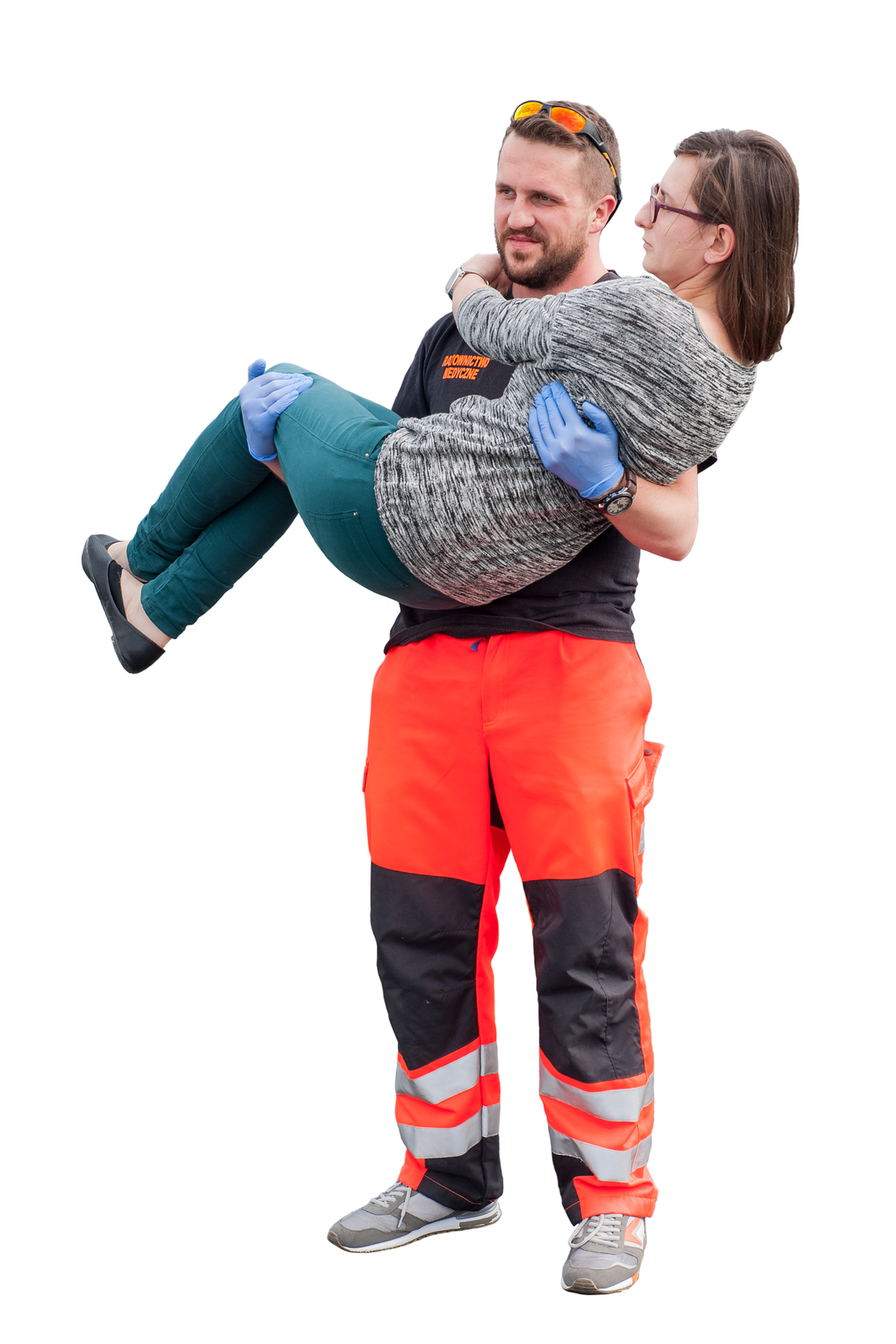 Na ilustracji numer dwa ratownik ubrany w pomarańczowo czarne spodnie z paskami odblaskowymi poniżej kolan niesie poszkodowaną kobietę na rękach. Kobieta obejmuje rękami szyję ratownika, jest to tak zwany sposób matczyny.