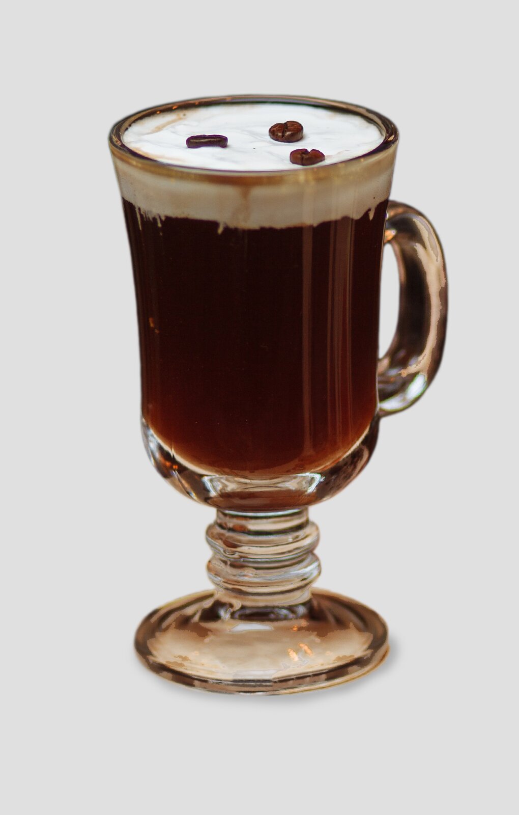 Ilustracja przedstawiająca wysoką szklankę, w której znajduje się ciemnobrązowy płyn. Na górze widoczna jest warstwa pianki oraz ziarna kawy.