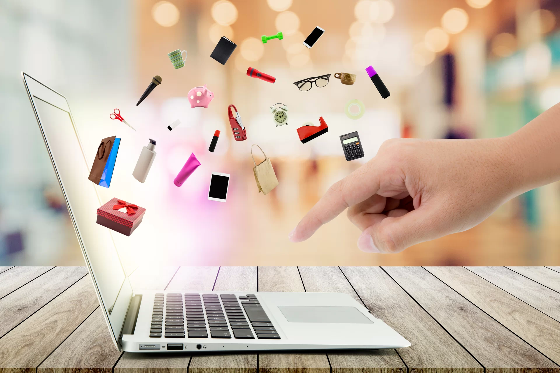 Ilustracja przedstawia zakupy przez Internet. Po prawej stronie wyłania się dłoń, która kieruje się w stronę klawiatury laptopa. Z ekranu wypływają ikony takie jak: nożyczki, mikrofon, kubek, skarbonka, scyzoryk, telefon, torba, kalkulator, mazak, okulary, ciężarek, latarka.