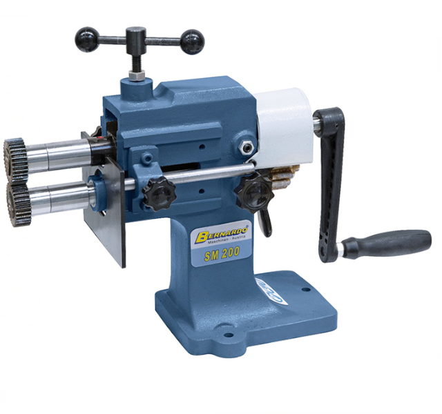 Ilustracja przedstawia żłobiarkę do blachy. Urządzenie składa się z korbki oraz dwóch wałków zakończonych nakrętkami. W górnej części urządzenia widoczny jest docisk. 