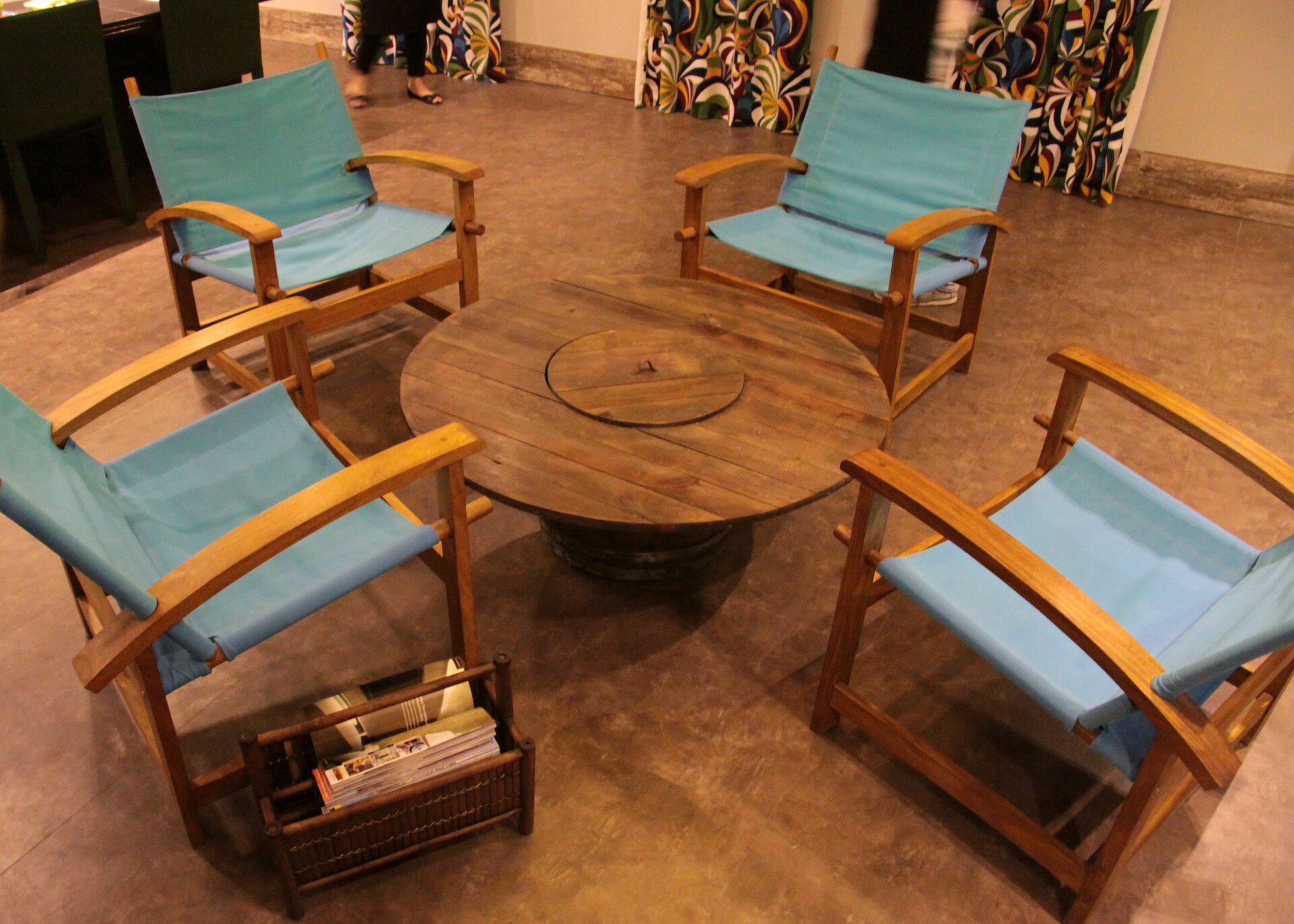 Na zdjęciu widoczny jest przykład powtórnego wykorzystania przedmiotów. Szpula do kabli energetycznych wykorzystana jest jako stół. Dookoła niej ustawione są cztery odrestaurowane fotele. Obok jednego z nich stoi gazetnik. Na podłodze parkiet, w tle ściany pomieszczenia.