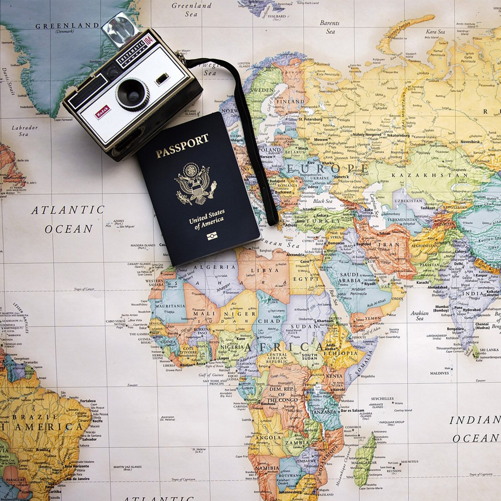 Zdjęcie przedstawia mapę, na której widoczne są następujący kontynenty: Europa, Azja i  Afryka oraz część Australii, Ameryki Południowej, Ameryki Północnej. Na mapie leży aparat i paszport. 