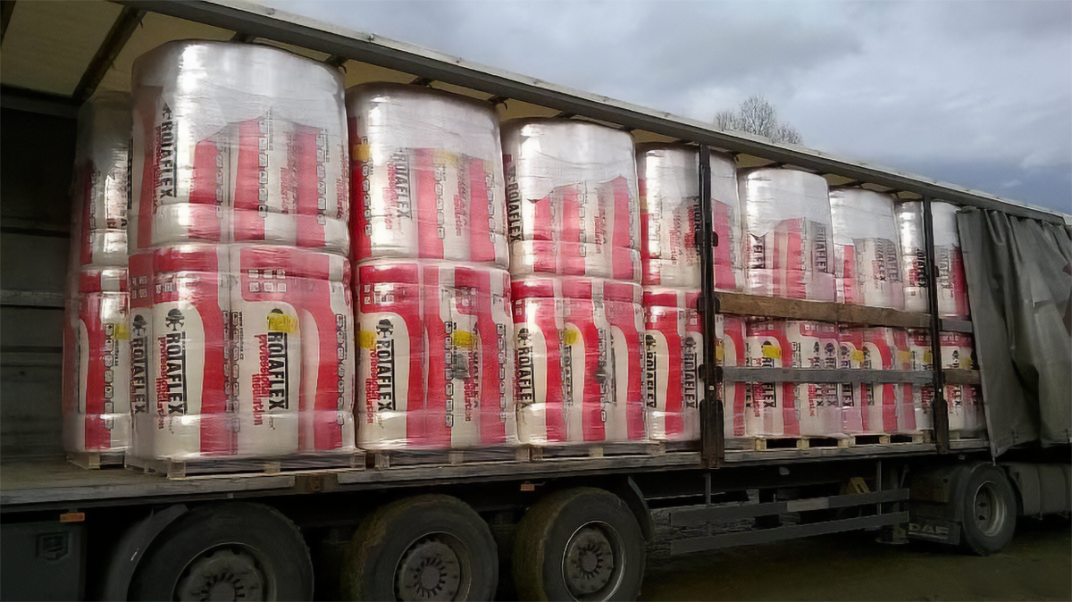 Transport waty szklanej. Zdjęcie przedstawia ciężarówkę załadowaną dużymi rolkami waty szklanej, poukładanymi zwarto.