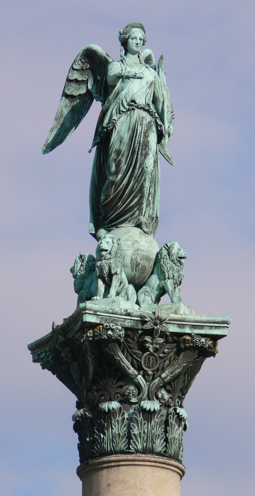 Zdjęcie przedstawia rzeźbę bogini zgody, która ubrana jest w długą szatę. Kobieta ma skrzydła, a w rękach trzyma róg oraz wianek. Stoi na kuli, która podtrzymywana jest na grzbietach trzech lwów. Dolna część rzeźby jest zdobiona w kwiaty oraz owoce. Rzeźba ma zielonkawy kolor. W tle zdjęcia znajduje się błękitne niebo.