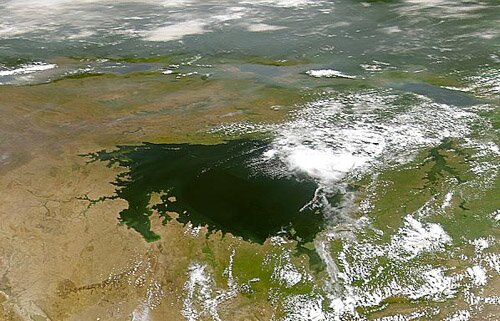 Zdjęcie satelitarne przedstawia zbiornik wodny. Kolor wody jest zielony. Zbiornik ma kształt zbliżony do koła. Teren wokół jeziora ma kolor brązowy, miejscami jest zielonkawy.  