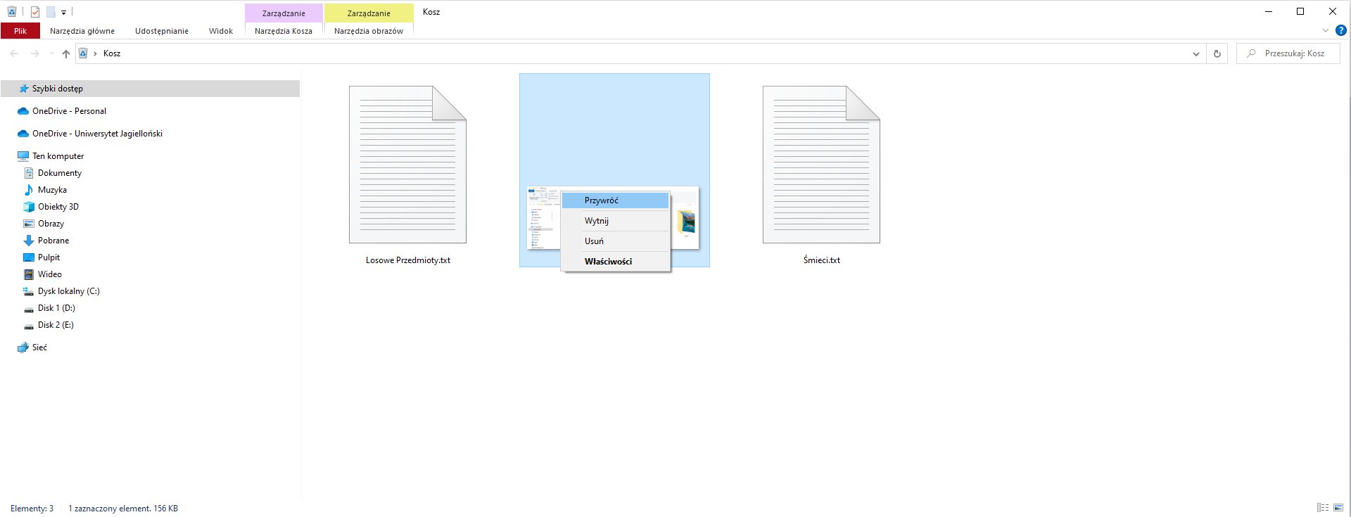 Zrzut ekranu Eksploratora plików z otwartym folderem koszem. W prawym górnym rogu znajduje się nazwa bieżącego otwartego folderu "Moje prace", poniżej znajdują się zakładki "Pliki", "Narzędzia główne", "Udostępnianie", "Widok" oraz dwie zakładki zarządzania "Narzędzia Kosza", "Narzędzia obrazów". W drzewie folderów po lewej stronie znajdują się "Szybki dostęp",  "OneDrive - Personal", "OneDrive - Uniwersytet Jagielloński" oraz "Ten komputer" - "Dokumenty", "Muzyka", "Obiekty 3D", "Obrazy", "Pulpit", "Wideo", "Dysk lokalny (C:)", "Disk 1 (D:), "Disk 2 (E:)", "Sieć". W koszu znajdują się pliki "Losowe Przedmioty.txt", "Śmieci.txt" oraz zaznaczone zdjęcie z aktywnym menu kontekstowym. W menu kontekstowym dostępne są opcje "Przywróć" (podświetlony), "Wytnij", "Usuń", "Właściwości". 