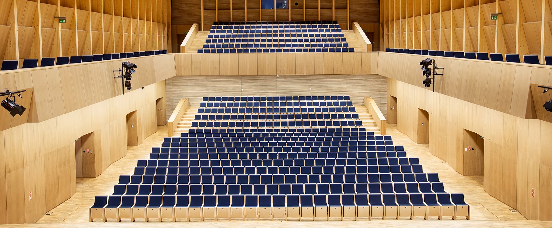 Fotografia przedstawia wnętrze sali koncertowej, w której widownia może słuchać koncertu na dwóch poziomach - dolnym oraz górnym. Sala ma bardzo jasny wystrój - składający się z jasnej drewnianej podłogi oraz ścian obitych drewnem. Na ścianach wiszą lampy doświetlające wnętrze. 
