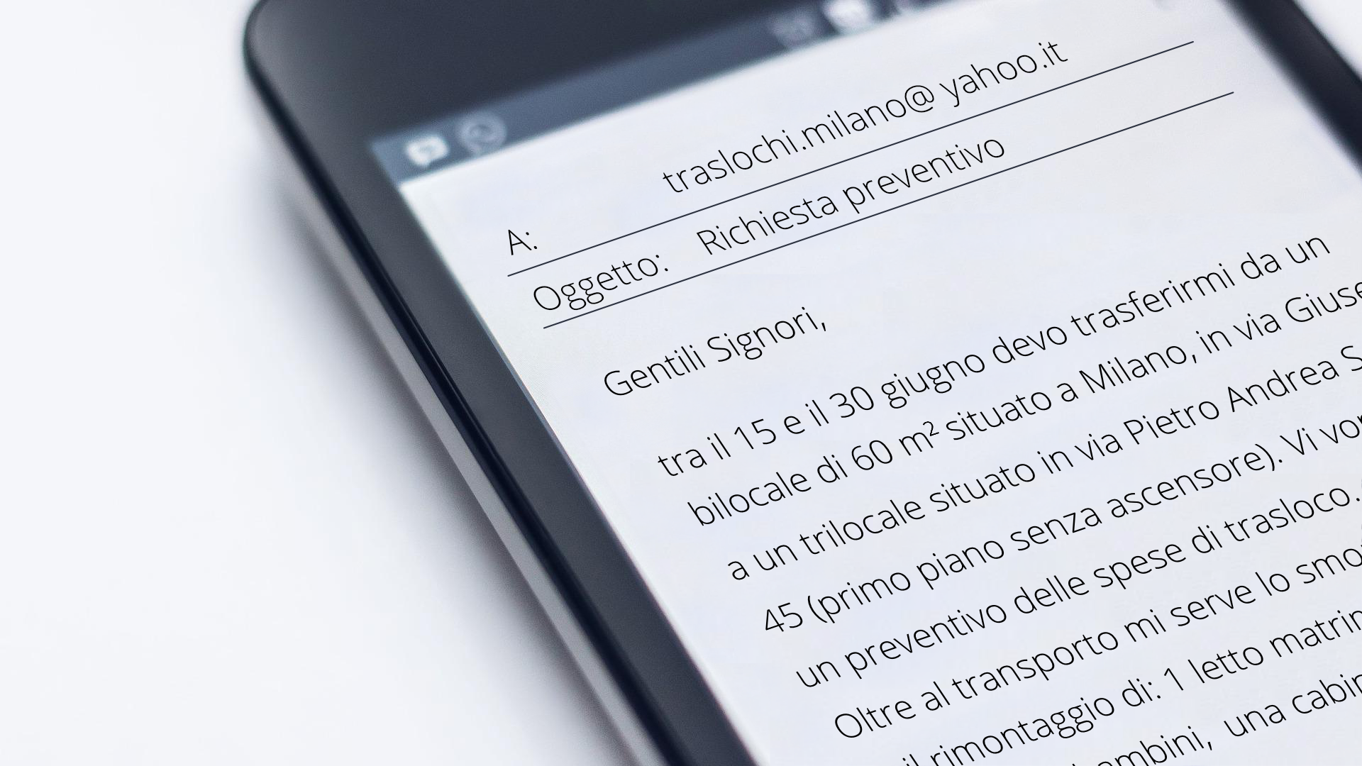 Zdjęcie przedstawia fragment telefonu komórkowego lub tabletu. Na ekranie wyświetlony jest mail do firmy zajmującej się przeprowadzką. Na górze maila znajduje się adresat i tytuł maila: A: traslochi.milano@yahoo.it, Oggetto: Richiesta preventivo. Poniżej widoczna jest treść maila.