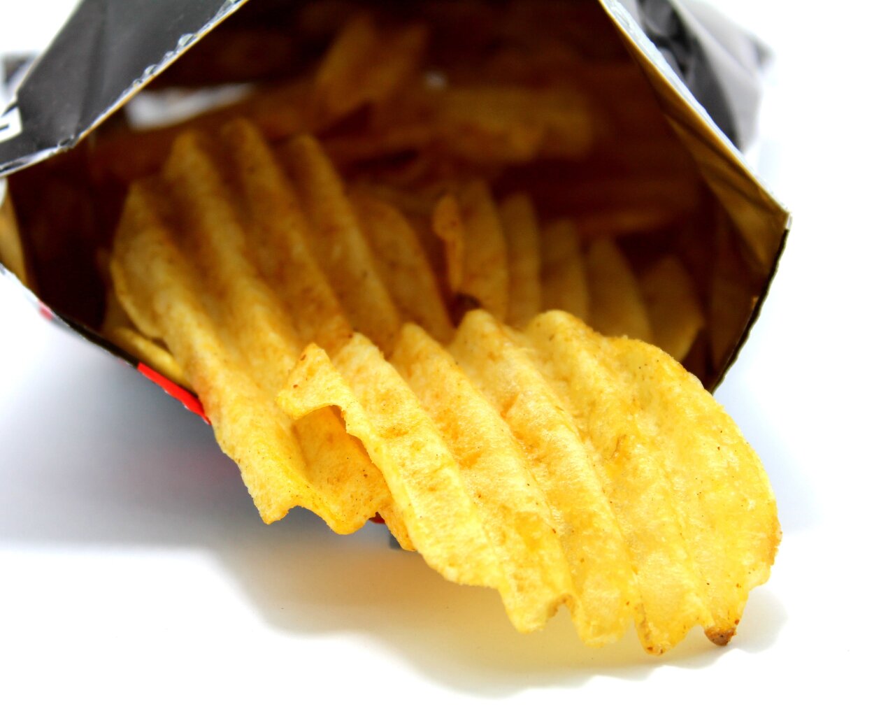 Zdjęcie przedstawia karbowane chipsy. Wysypują się z paczki. 