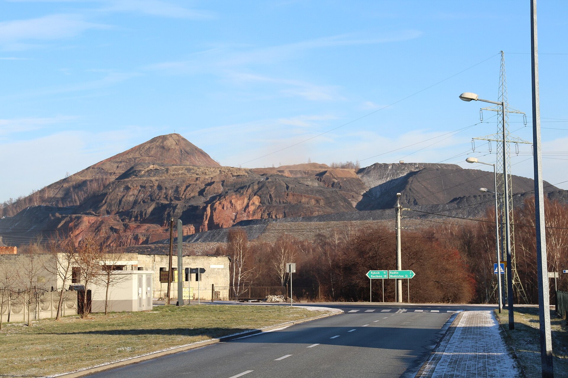 Na fotografii na pierwszym planie asfaltowa ulica, w tle ogromna hałda w odcieniach koloru brązowego. Posiada strome stoki, jest rozległa, szeroka i masywna.