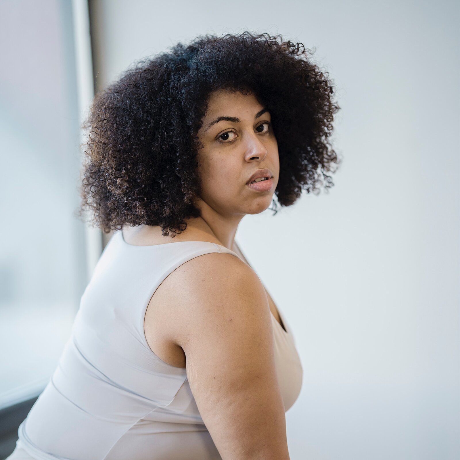 Zdjęcie przedstawia pozującą do zdjęcia, grubszą kobietę o krótkich, czarnych, kręconych włosach i czarnych oczach.