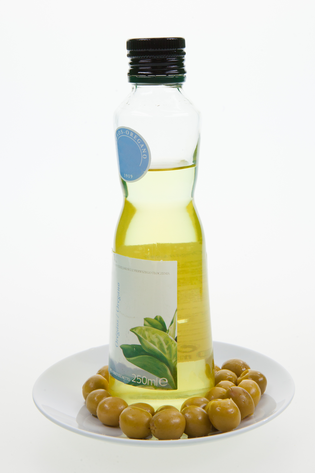 Fotografia przedstawiająca buteleczkę z oliwa z oliwek oraz rozłożone wokół niej liczne zielone oliwki