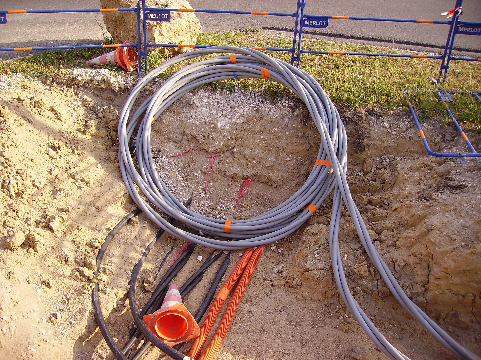 Na zdjęciu przedstawiony jest wykop wykonany na poboczu jezdni, w którym znajduje się duży zwój rur karbowanych, zwanych peszelami.