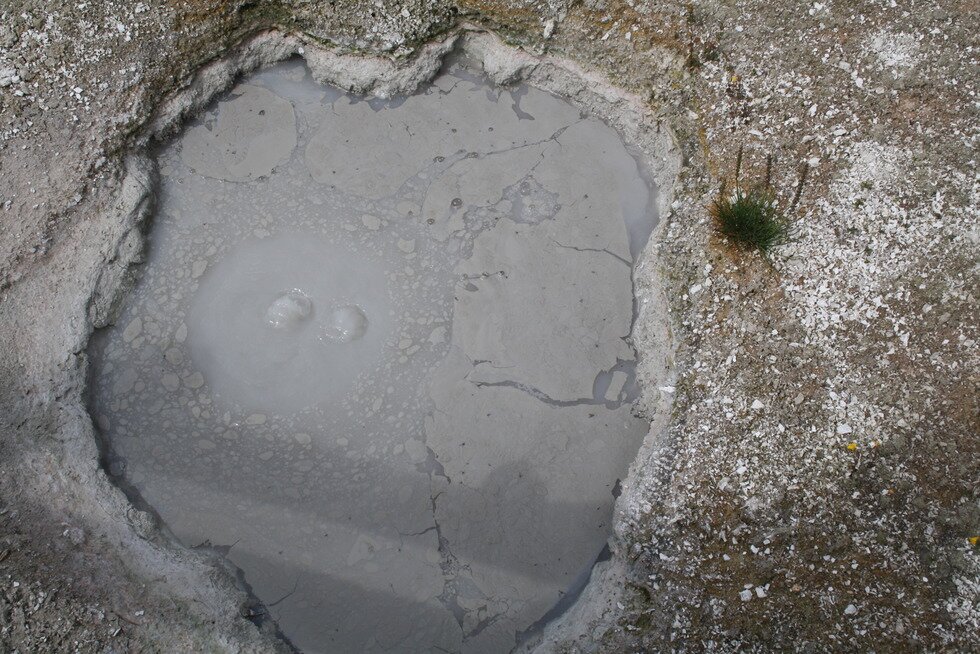 Na zdjęciu ukazano fumarolę. W zagłębieniu zebrała się brudna woda pokryta kożuchem, widoczne bąbelki gazu.