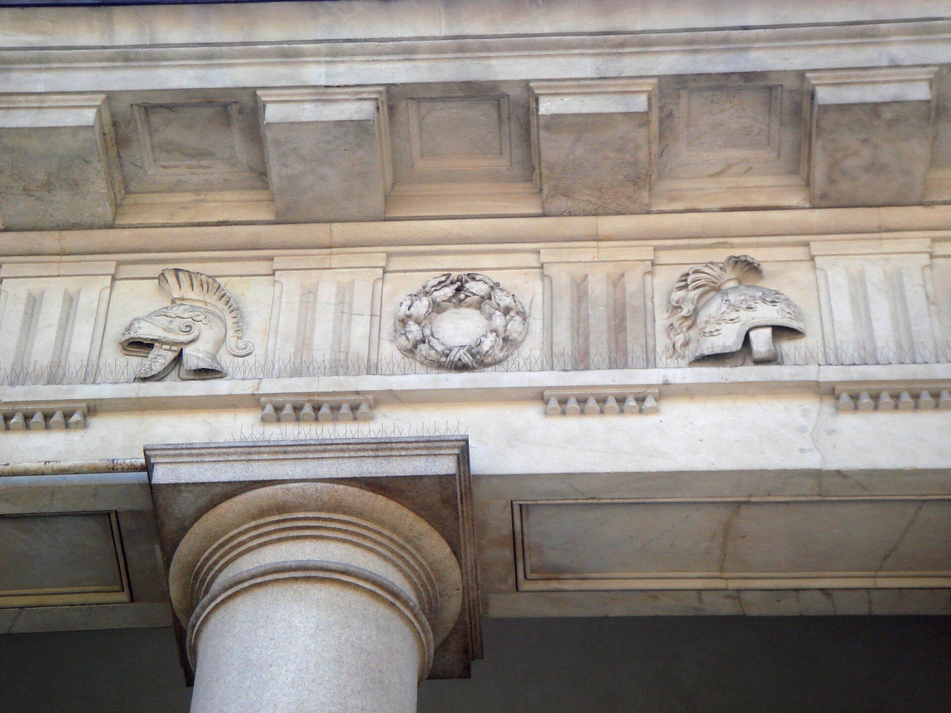 Na zdjęciu została przedstawiona część Porta Venezia znajdującej się w Mediolanie. Fotografia ukazuje fragment belkowania oraz górną część kolumny. Na ścianie, zrobionej z marmuru, znajdują się trzy wypukłe reliefy - jeden pośrodku, przedstawiający wieniec, oraz dwa przedstawiające widok boczny hełmu rzymskiego, znajdujące się po bokach pierwszego. Między nimi umieszczono elementy ze żłobieniami. Kolumna na dole jest gładka, zakończona kwadratowym elementem. Nad reliefami, na gzymsie, znajdują się wypukłe elementy dekoracyjne - kwadratowe bloki.