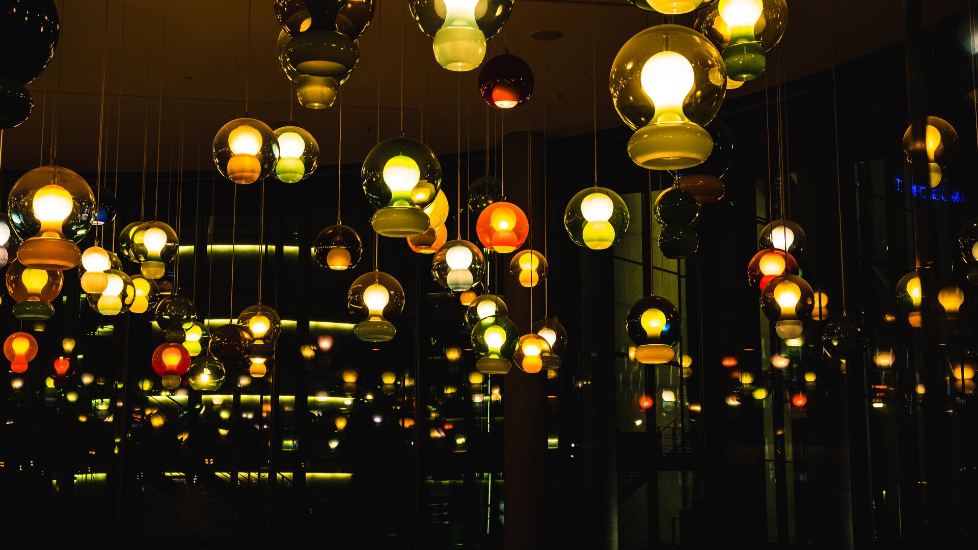 Na zdjęciu widocznych jest mnóstwo wiszących lamp o zbliżonych kształtach. Lampy mają szklany, kulisty klosz, wewnątrz którego widoczna jest zaświecona żarówka. Wszystkie lampy są zaświecone, więc są jasnymi punktami na prawie czarnym tle.