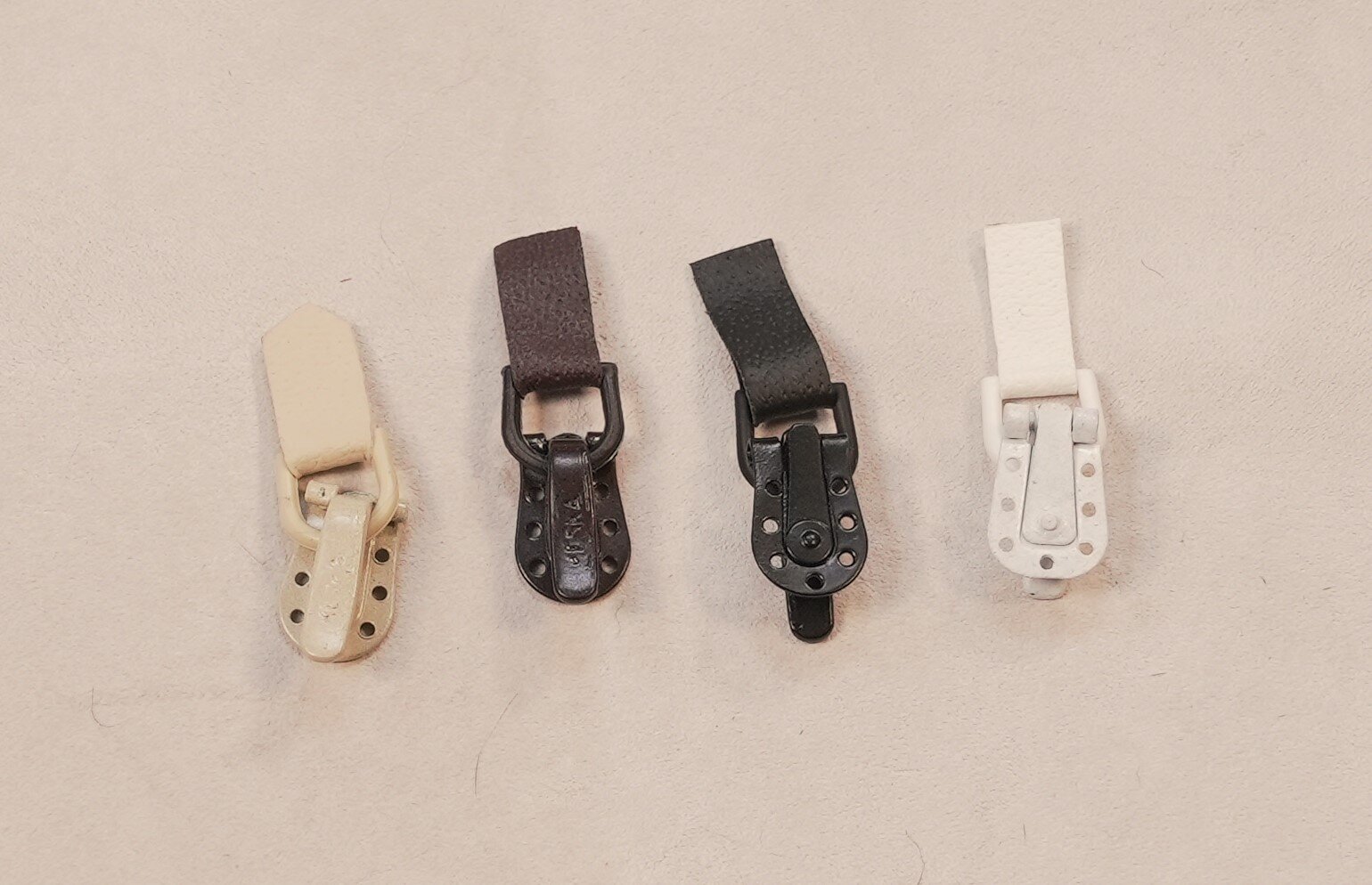 Na zdjęciu widoczne cztery umieszczone obok siebie metalowe zapięcia ze skórzanymi paskami.