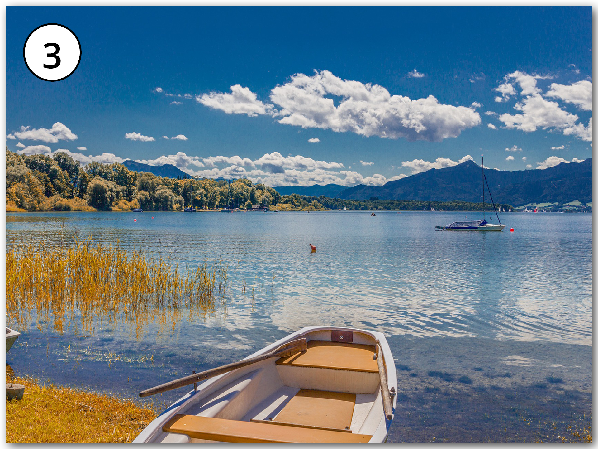 Grafika przedstawia widok na jezioro, po którym pływają łódki. W tle widoczne góry i las.