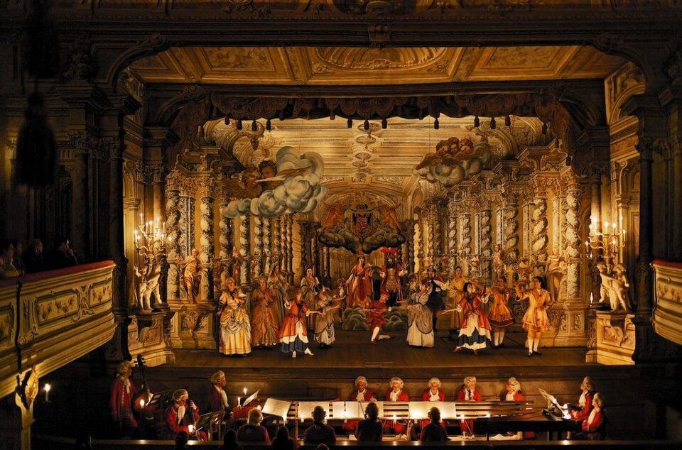 Zdjęcie przedstawia najlepiej zachowany na świecie teatr barokowy z XVIII wieku w Czeskim Krumlowie. Przepych dekoracji, złocone elementy widowni teatralnej, aksamitna kurtyna ze złotymi frędzlami, a także dworskie kostiumy z perukami, w których występuje orkiestra na proscenium i przede wszystkim repertuar na scenie -  wszystko to sprawia wrażenie, jakbyśmy przenieśli się w dawne czasy.