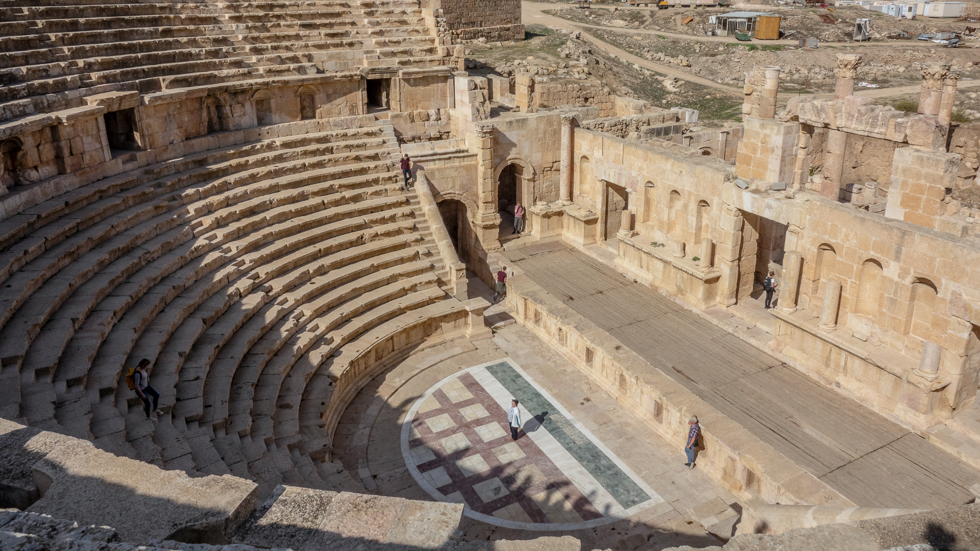 Zdjęcie przedstawia widok z góry na ruiny teatru greckiego. W centrum widoczne jest miejsce gdzie aktorzy występowali. Wokoło znajdują się miejsca dla widzów.