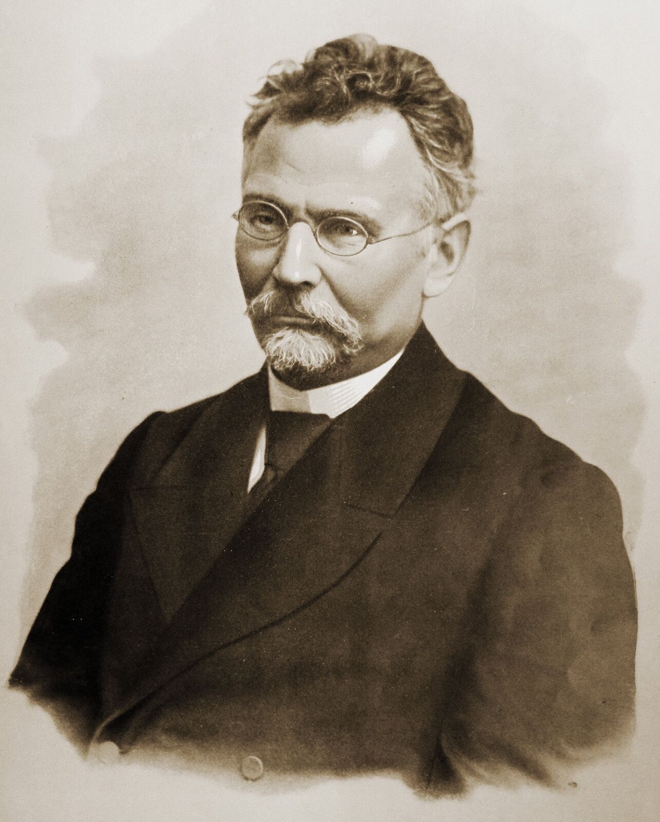 Kliknij, aby powiększyć. Zdjęcie Bolesława Prusa. Starszy mężczyzna w okularach z cienkimi oprawkami. Ma niewielką bródkę i wąsy, ubrany jest w ciemny surdut.