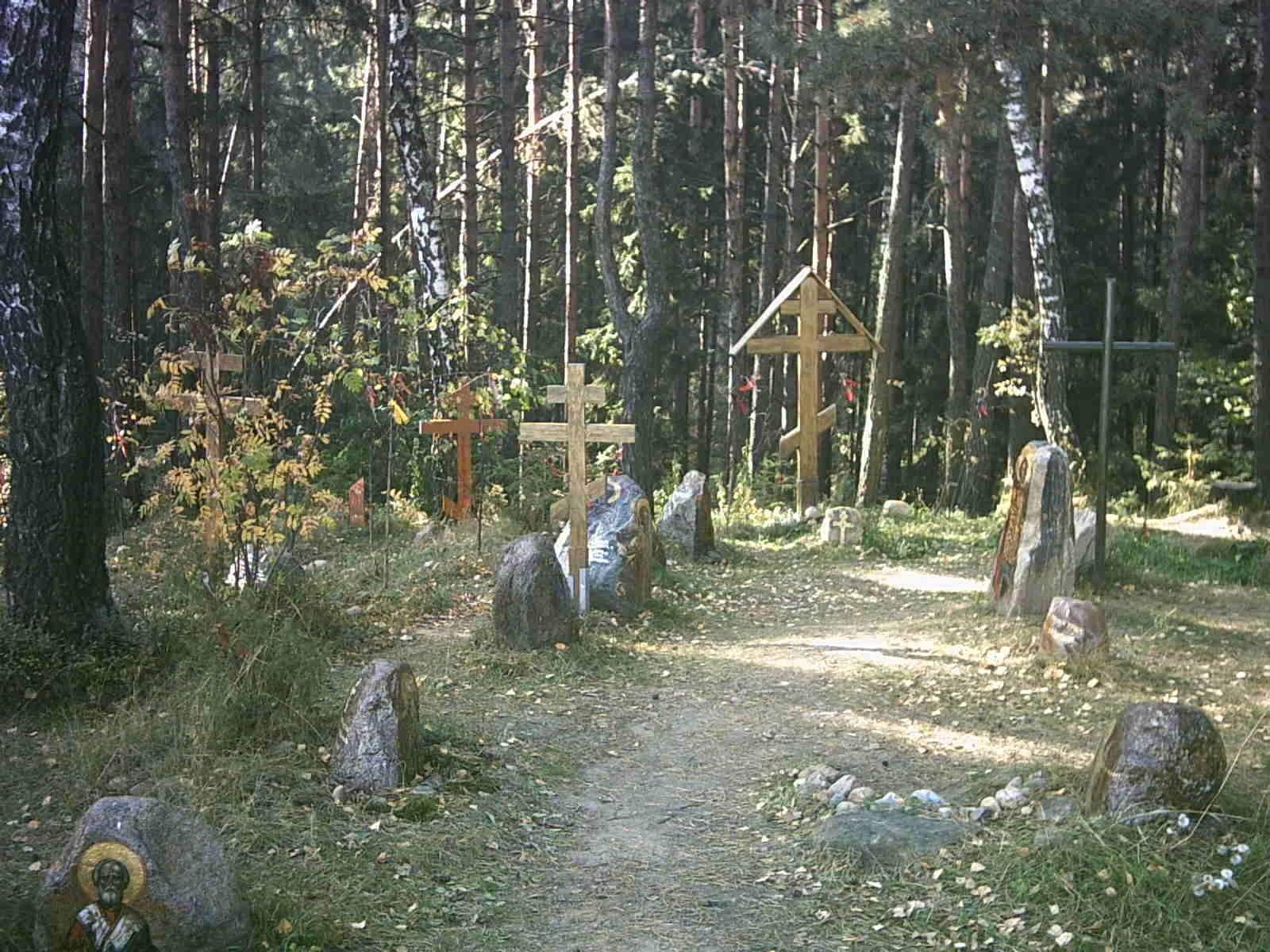 Na zdjęciu znajduje się leśny cmentarz. Pomiędzy kamieniami z podobiznami świętych znajdują się prawosławne drewniane krzyże.