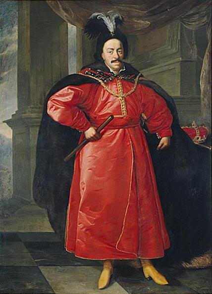 Ilustracja przedstawia portret Jana Kazimierza. Mężczyzna ubrany jest w długą czerwoną szatę ze złotymi guzikami, na nogach ma żółte buty, na plecach zarzuconą czarną pelerynę. Na głowie ma czarną czapkę z pióropuszem.