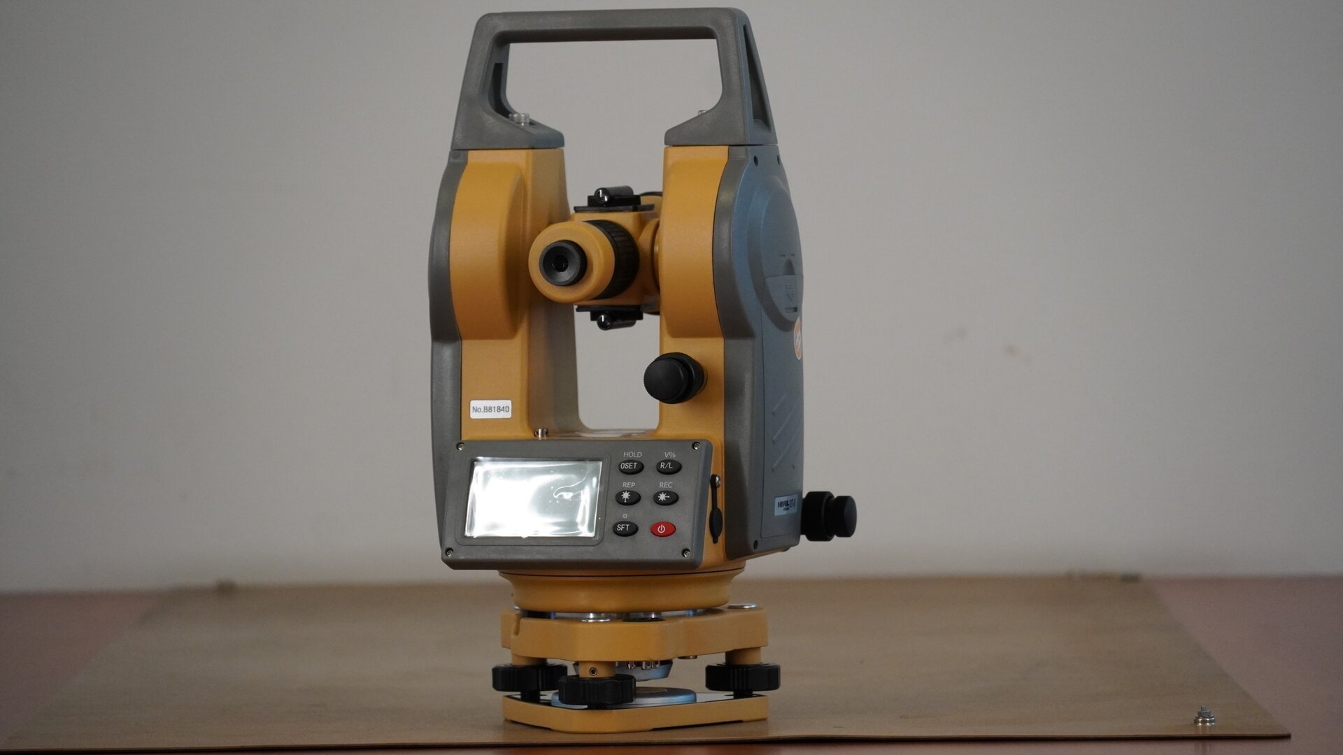 Na zdjęciu przedstawiono teodolit widziany od strony okularu. Urządzenie posiada trójkątną podstawę w formie płytki sprężynującej. W każdym jej rogu znajduje się śruba poziomująca. Na śrubach osadzona jest spodarka, czyli podstawa instrumentu. W spodarce mieści się śruba dociskowa, a na spodarce okrągła alidada, czyli korpus urządzenia. Na nim zaś znajdują się pokrętła leniwki alidady i leniwki lunety oraz zacisk alidady i lunety. Konstrukcję instrumentu uzupełnia prostokątna rama z uchwytem w górnej części. Pod okularem znajduje się wyświetlacz z przyciskami.