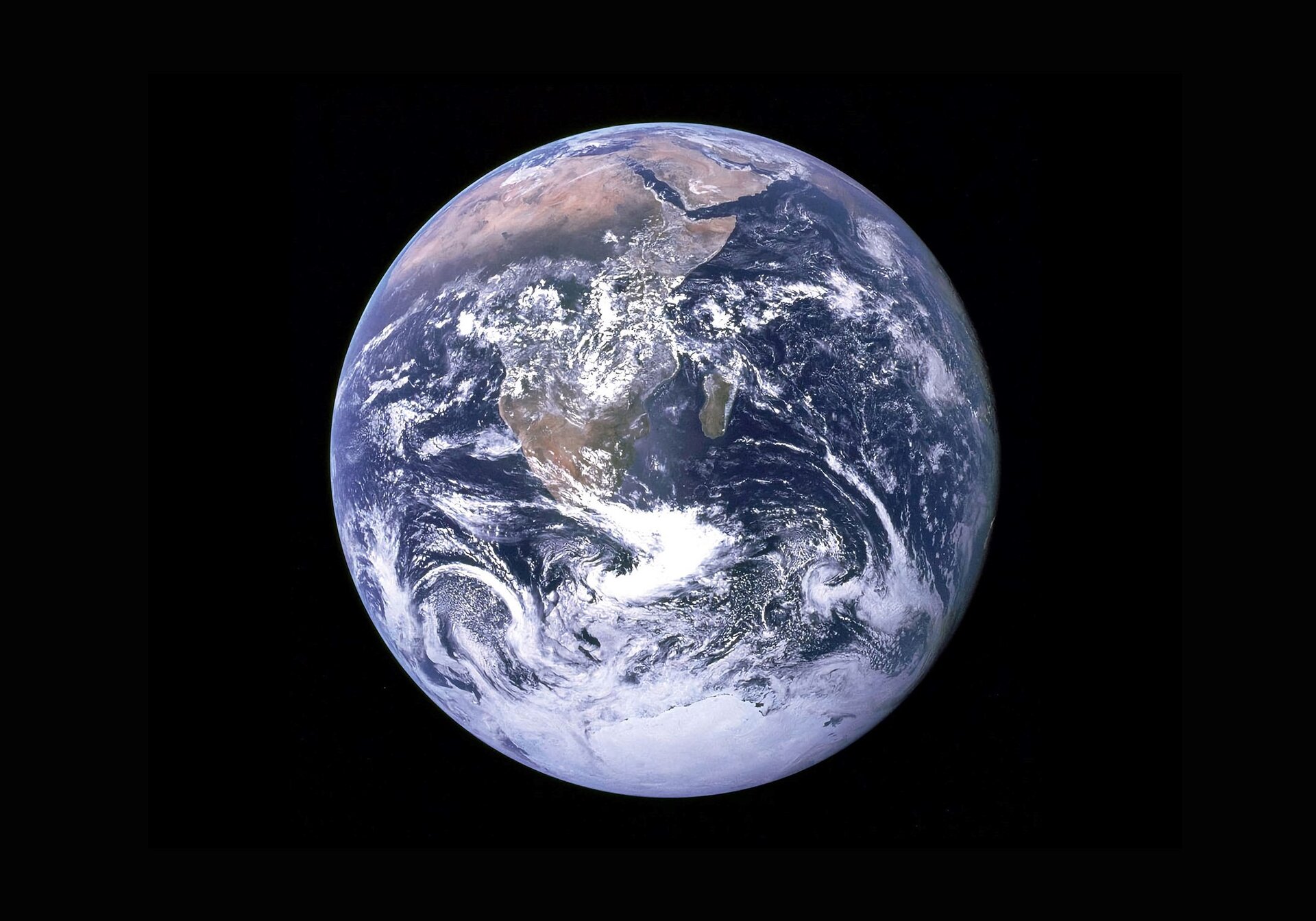 Zdjęcie przedstawia kulę ziemską widzianą z kosmosu, z widocznymi kontynentami i zbiornikami wodnymi oraz frakcjami białych chmur, które kłębią się nad częścią kontynentów.