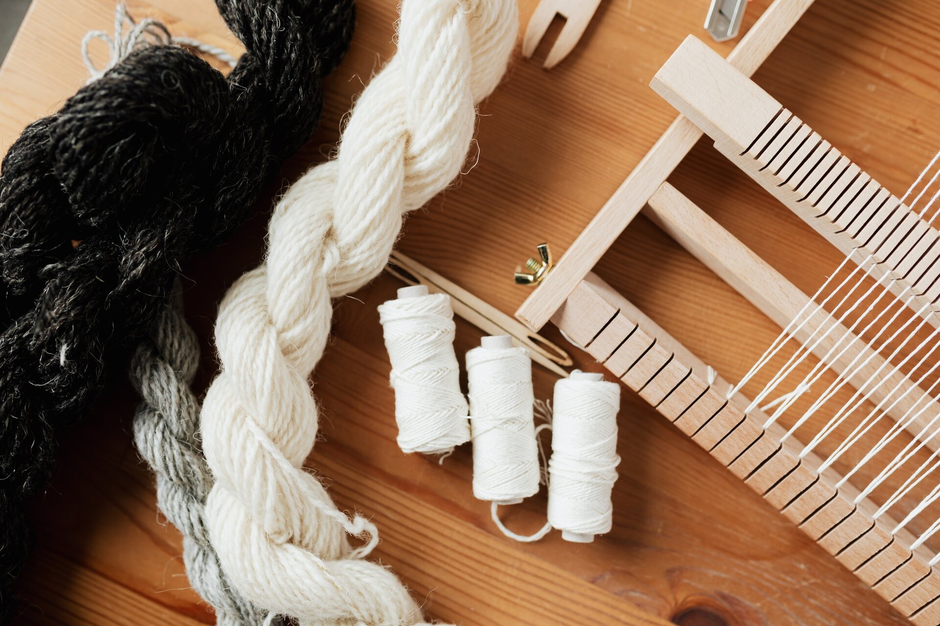 Na zdjęciu widoczne trzy szpule białej nici, krosno tkackie, czyli drewniana ramka, na którą nawleka się nić tak, by tworzyła pionowe pasy. Po lewej stronie znajduje się warkocz z białej nici, a obok czarna wełna. Nagranie tożsame z treścią.