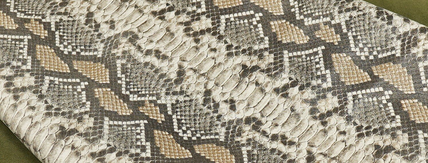 Zdjęcie przedstawia zbliżenie na skórę węża. Skóra pokryta jest łuskami w różnych odcieniach brązu i beżu. 
