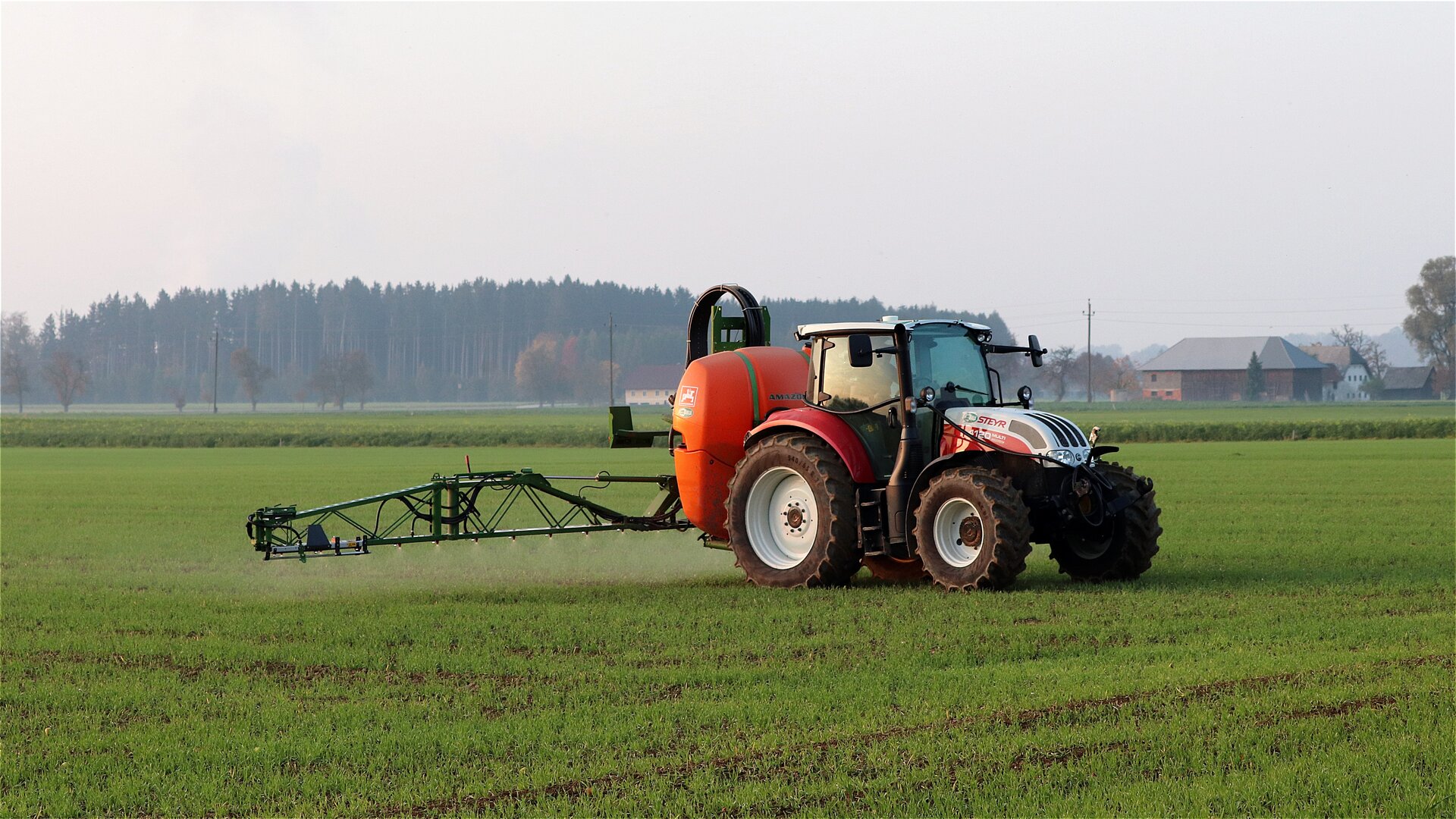 Zdjęcie czwarte przedstawia opryskiwacz przymocowany do tyłu ciągnika jadącego po polu. Z opryskiwacza wydobywa się rozproszony strumień płynu.