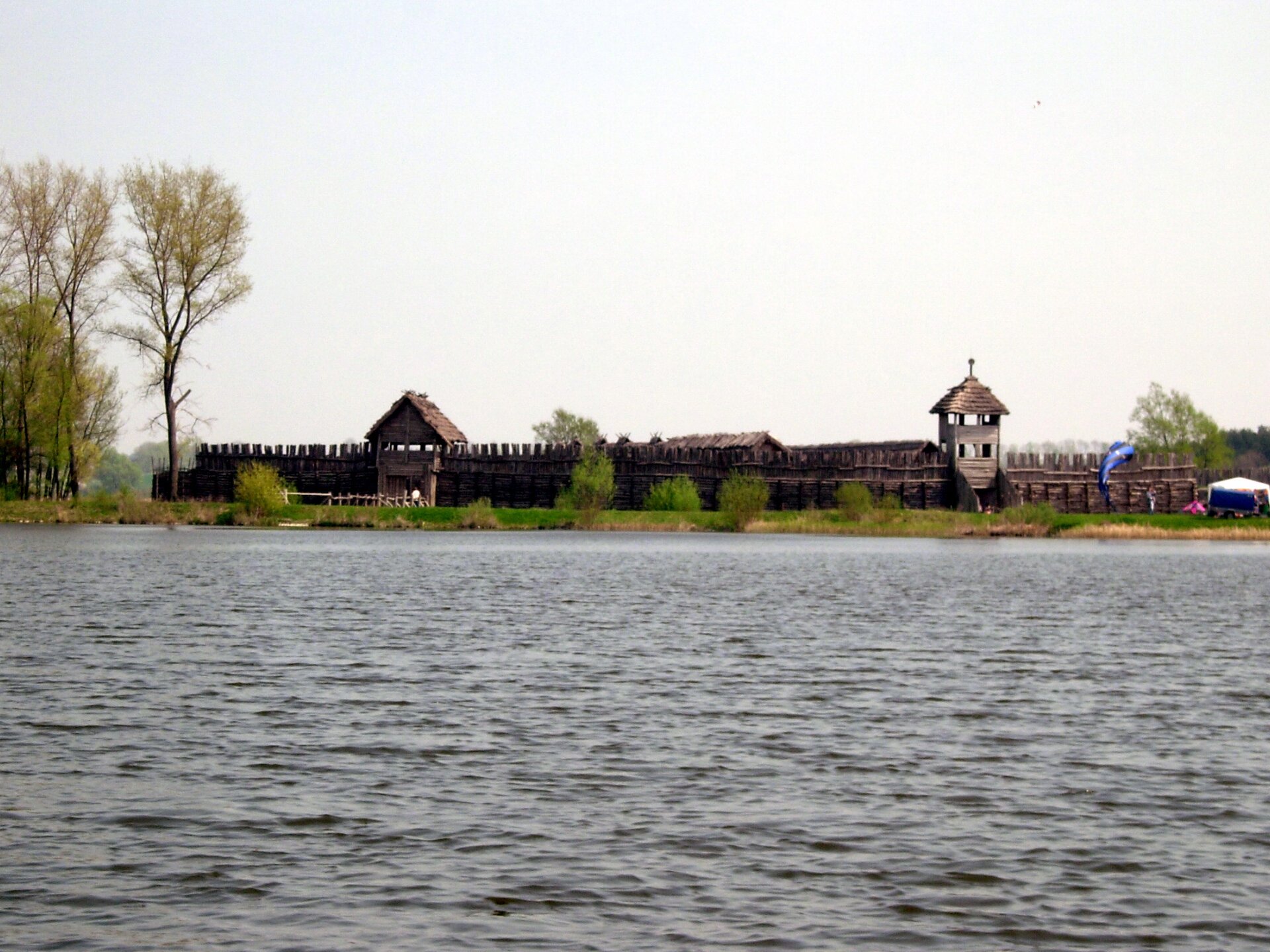  Zdjęcie przedstawia osadę nad jeziorem. Widać dwie wieże i palisadę. 