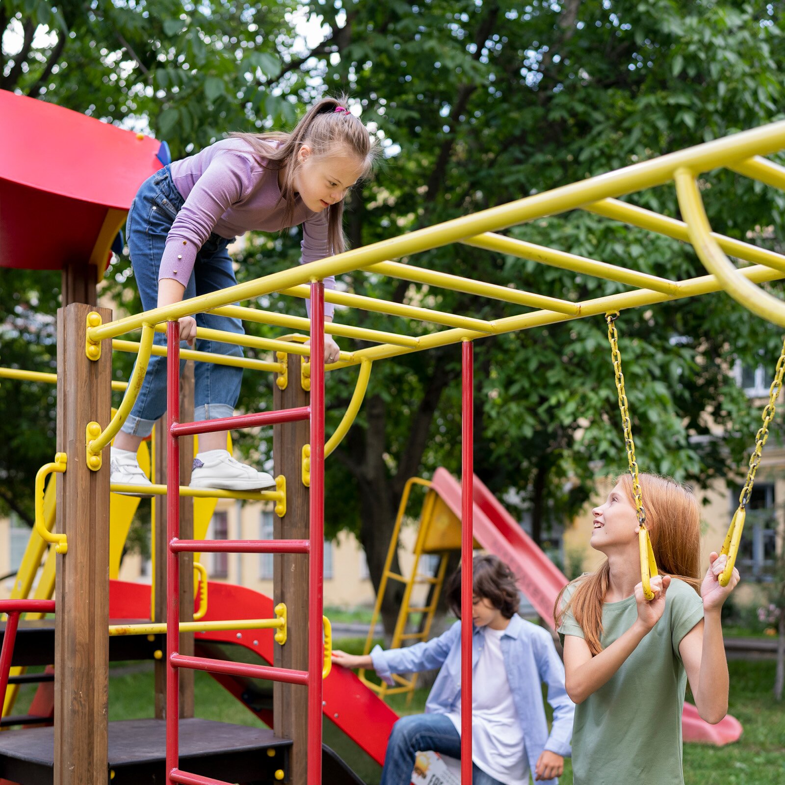 Na zdjęciu widać plac zabaw w parku, z drabinkami, drążkami, zjeżdżalniami i kółeczkami do podciągania się. Na placu widzimy troje dzieci w wieku szkolnym - dwie dziewczyny i chłopca.