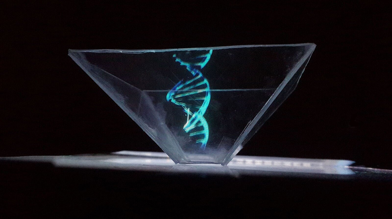 Grafika przedstawia wirującą spiralę DNA na odwróconej, piramidalnej konstrukcji położonej na wyświetlaczu telefonu.