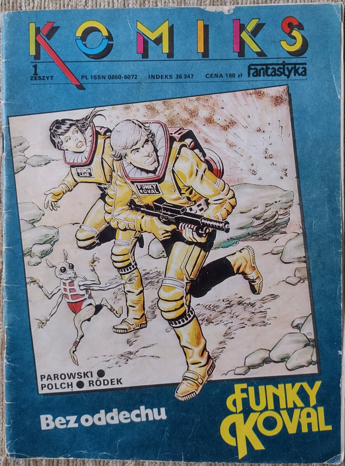 Zdjęcie czasopisma. W górnej części okładki znajduje się napis „komiks”. W środkowej części ilustracja na której jest kobieta i mężczyzna. Para ubrana jest w żółte kombinezony kosmiczne. Mężczyzna trzyma w ręku broń. Przed postaciami znajduje się kosmiczny stworek ubrany w czerwony kombinezon. Tło okładki jest niebieskie.