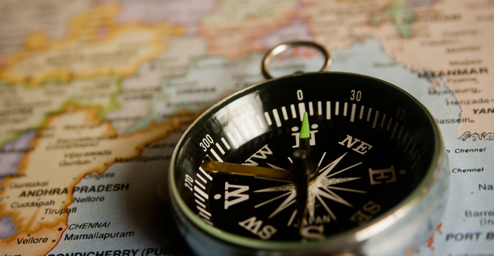 Na zdjęciu znajduje się czarny kompas na tle dużej mapy.  Kompas wskazuje północ. Na szczycie kompasu kółko umożliwiające przywiązanie sznurka.